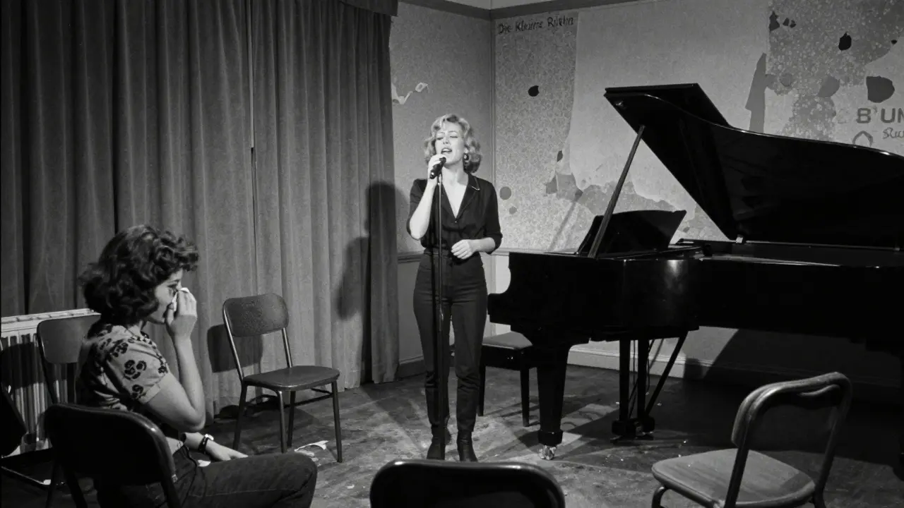 Black-and-white photo of Sibylle Rauch performing on a small stool in a cramped basement venue, audience member crying.